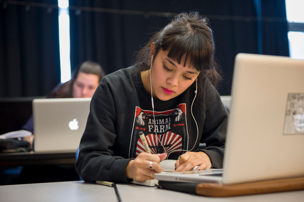 A graphic design student in a classroom at RRC Polytech taking notes on a notebook