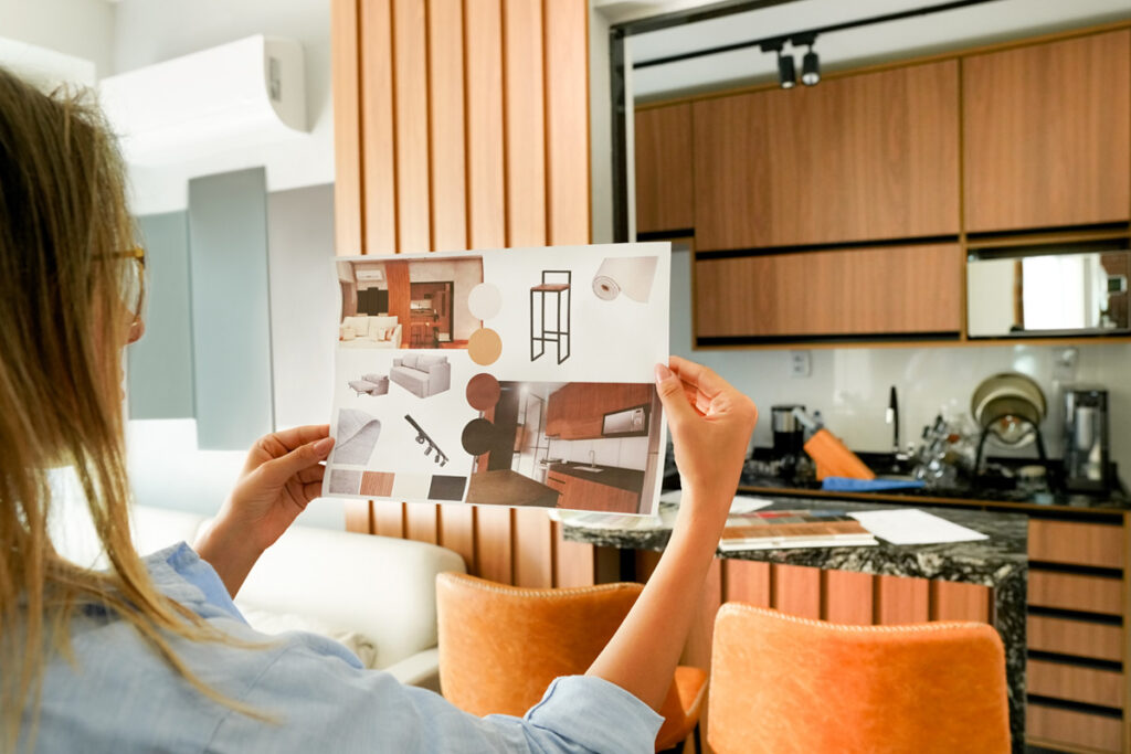 Over the shoulder view of a female looking at the picture of interior design sitting at home office.