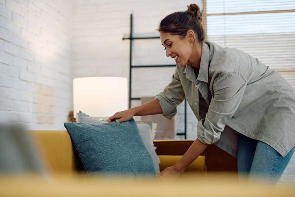Young happy woman arranging the cushions on her couch.