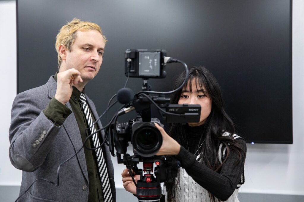 Entertainment production graduate working on a film set, adjusting lighting equipment during a professional shoot.