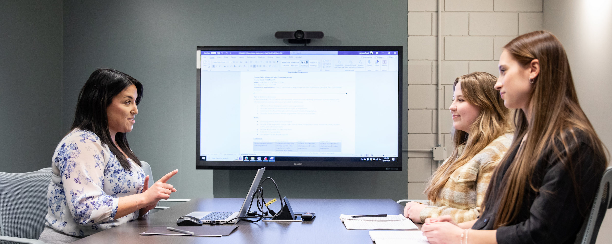 Instructor leading a small group discussion with students in a meeting room with large display screen