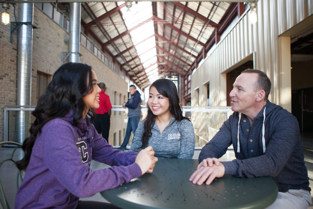 Students and instructor having an engaging conversation in a modern campus corridor with skylights