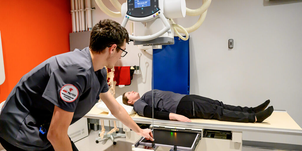 Radiography student positioning a patient for an X-ray in a clinical training lab.