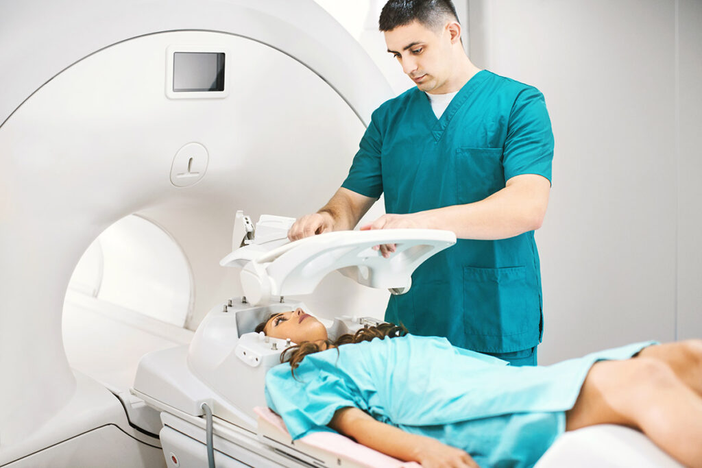 Young female patient lying on back while technician positioning safety equipment on her head for brain MRI scan.