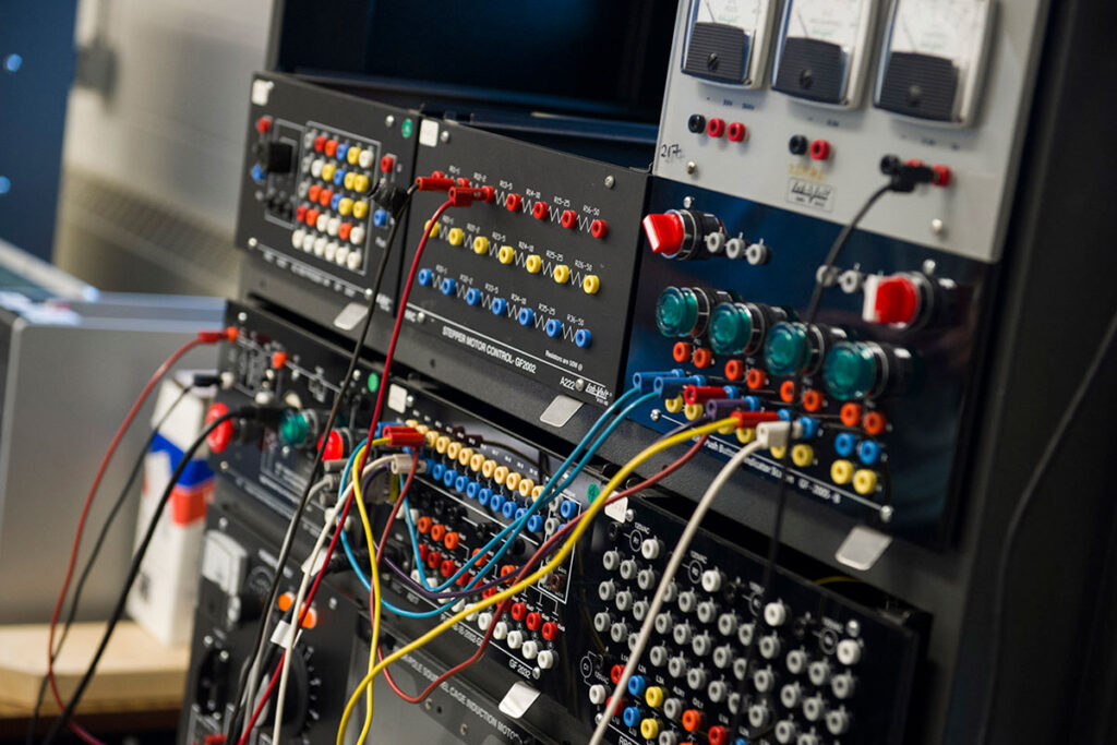 Close-up of a complex electronics training panel featuring stepper motor control modules, coloured terminal connectors, indicator lights, wires, and various industrial control components.