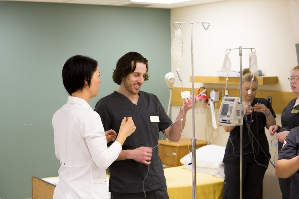 Nursing student practices intravenous therapy procedures under instructor supervision.