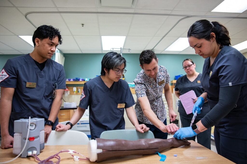 Nursing students receive instruction while practicing clinical procedures using a simulation training model.