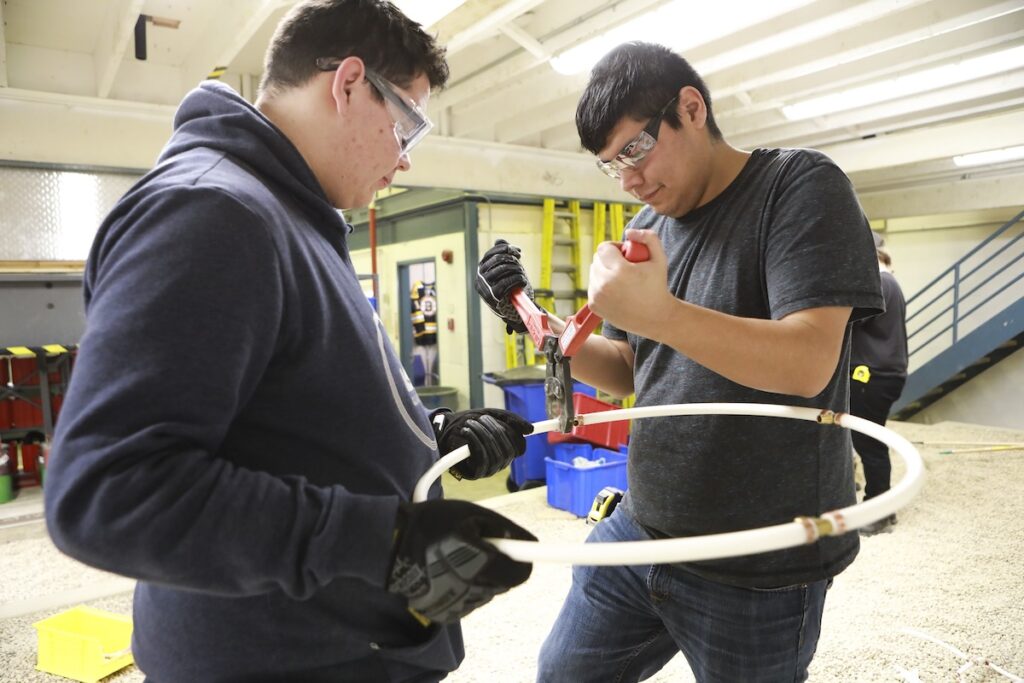 Students use a pipe cutter to prepare plastic piping during a hands-on plumbing lab.