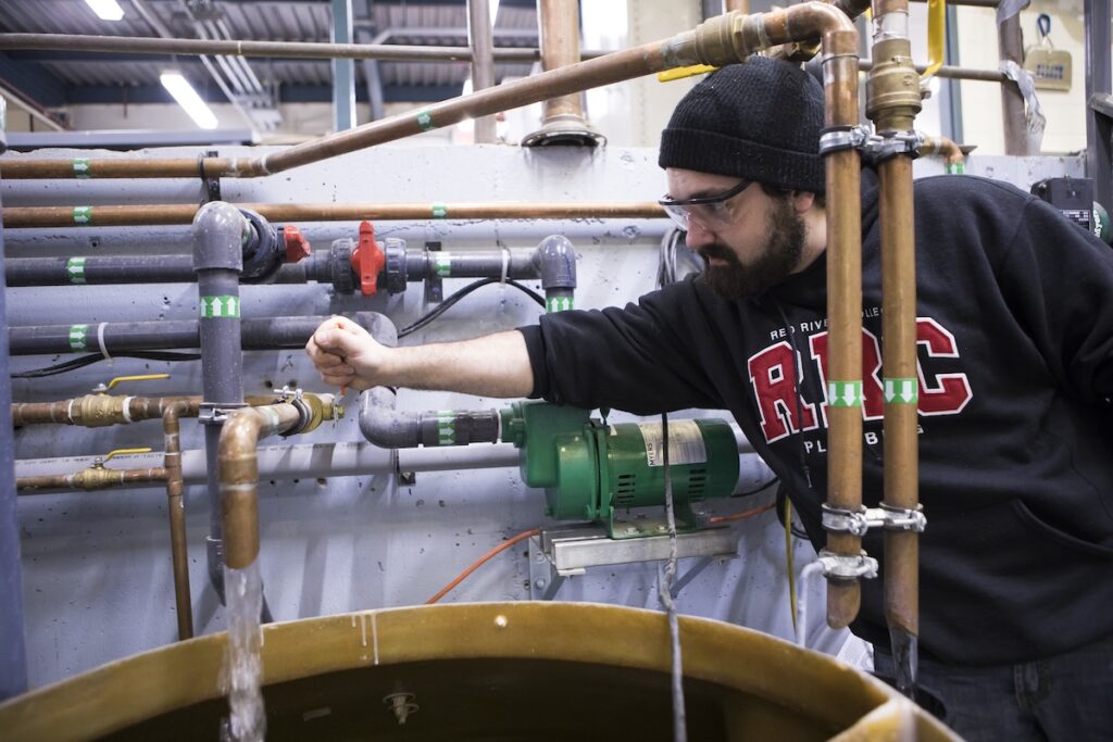 Piping trades student inspects and adjusts valves and pumps on a mechanical training system.