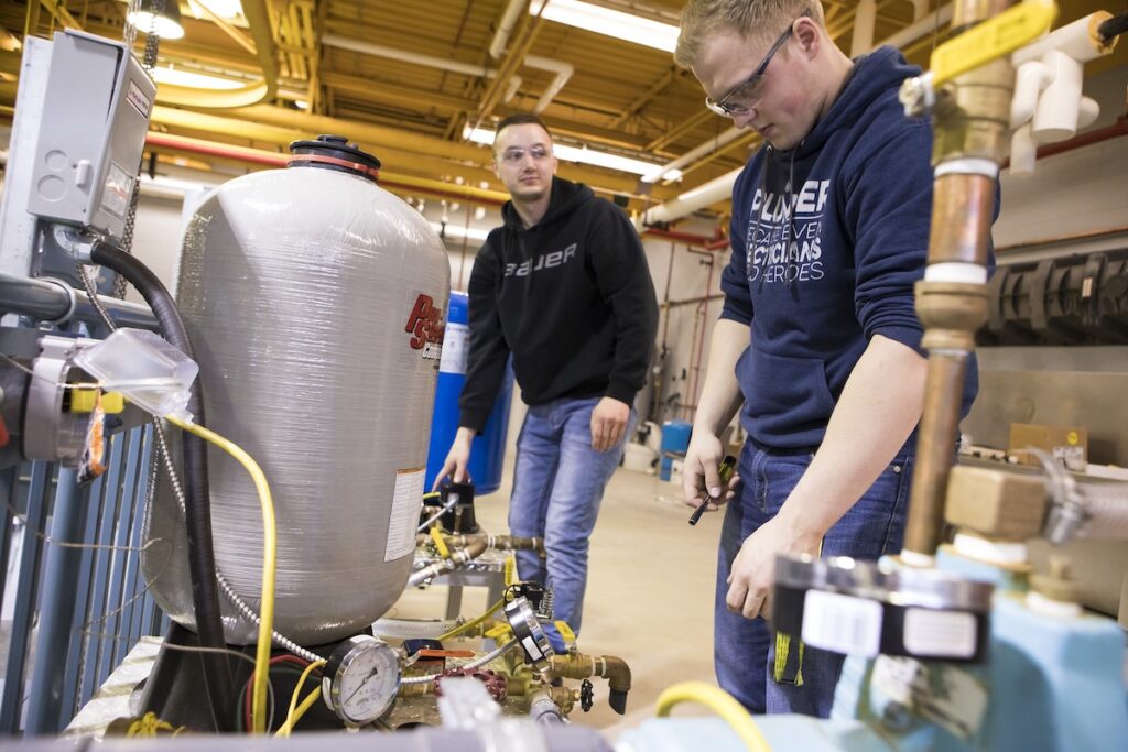 Students inspect and test components of a mechanical piping system during a laboratory exercise.