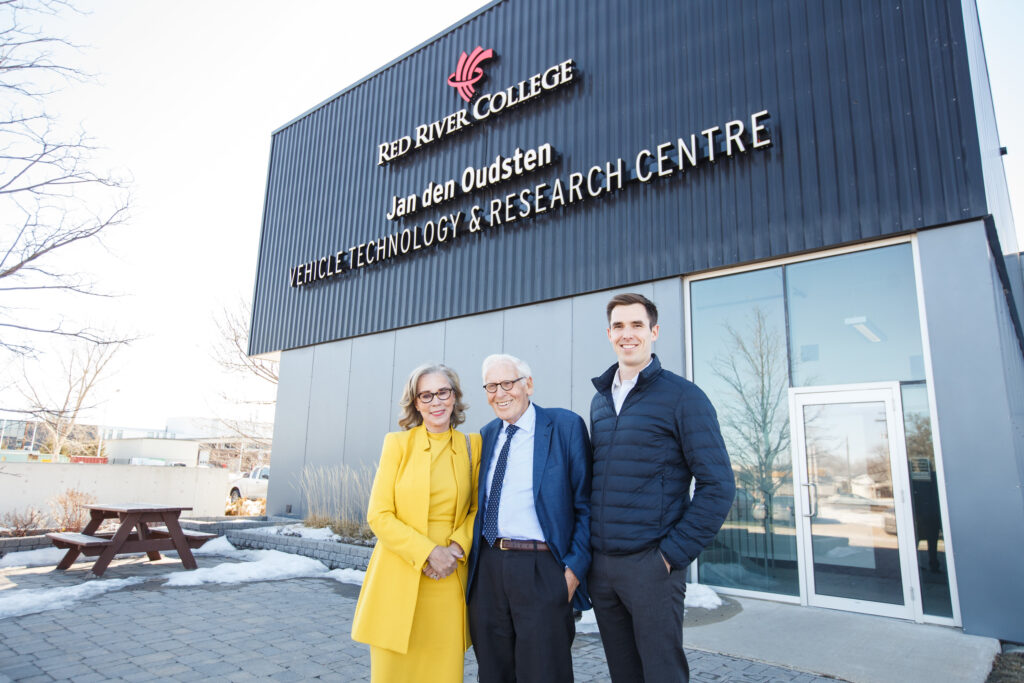Jan den Oudsten standing outside of the building named after him at RRC Polytech. He stands with his wife and son.