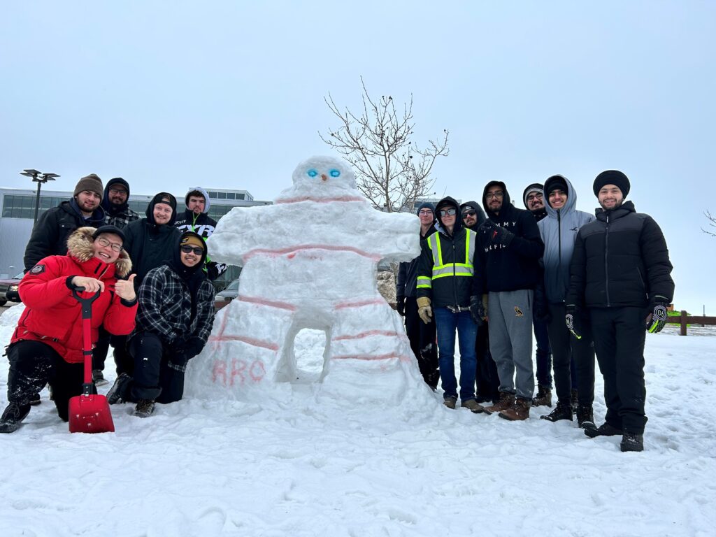 A group of students stand around their snow sculpture.