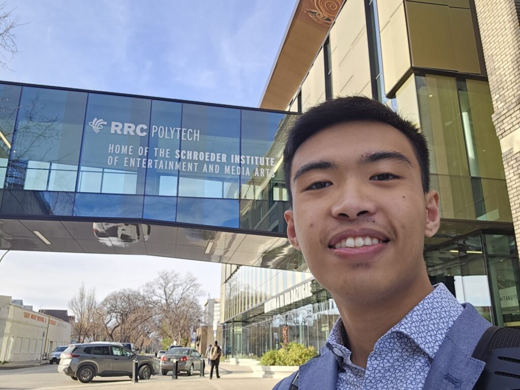 A selfie of a person wearing a blue shirt, standing in front of RRC Polytech's Exchange District Campus.