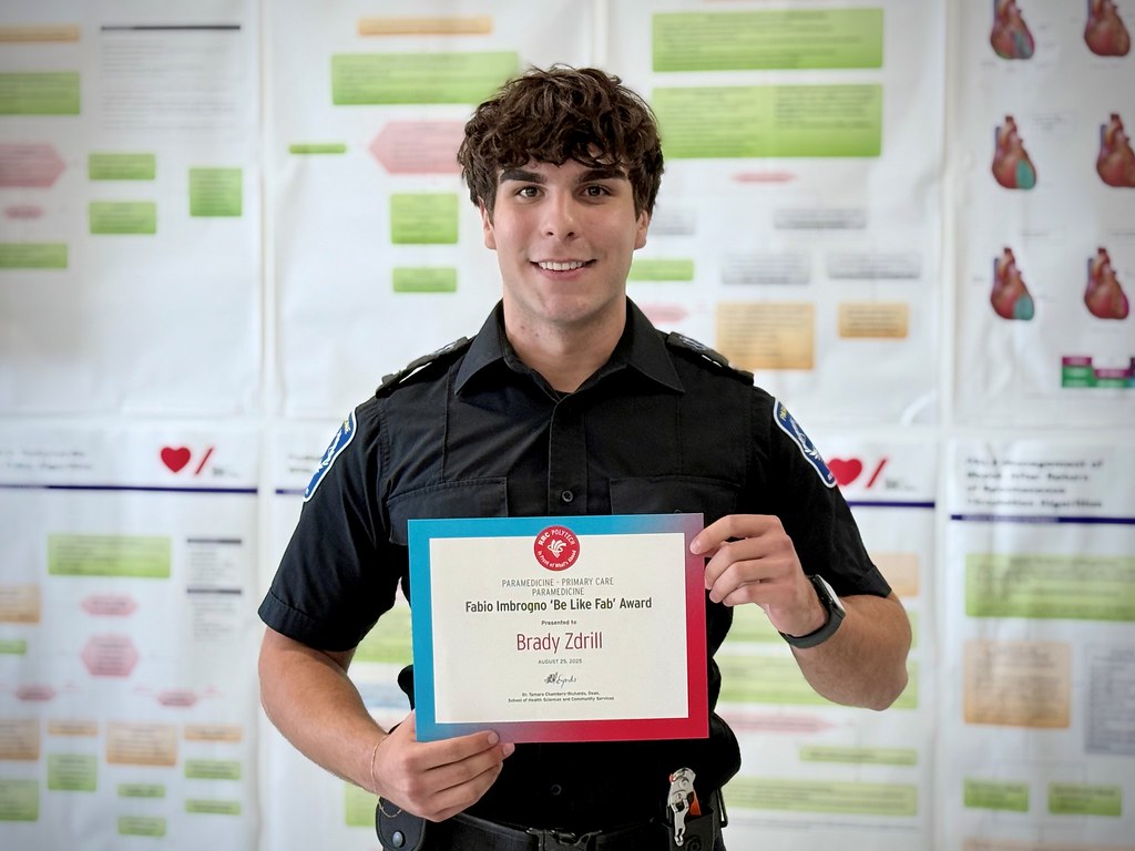 A person wearing a paramedic uniform holds a certificate and smiles.