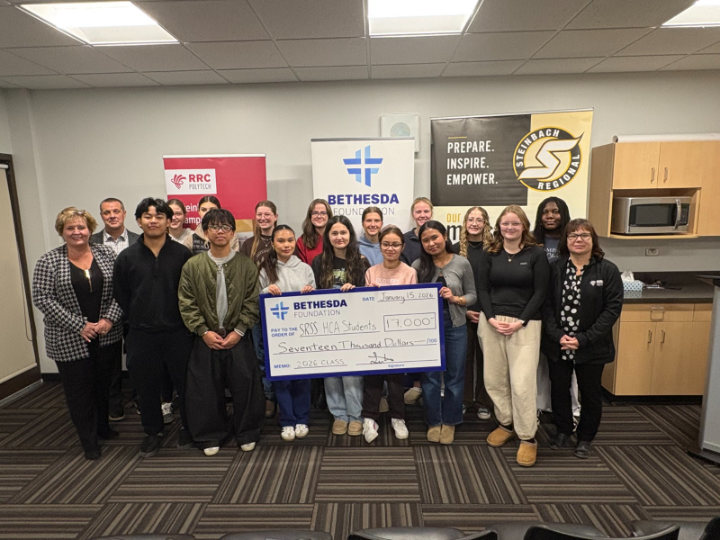 A group of people stand together, with people in the front row holding a large novelty cheque.