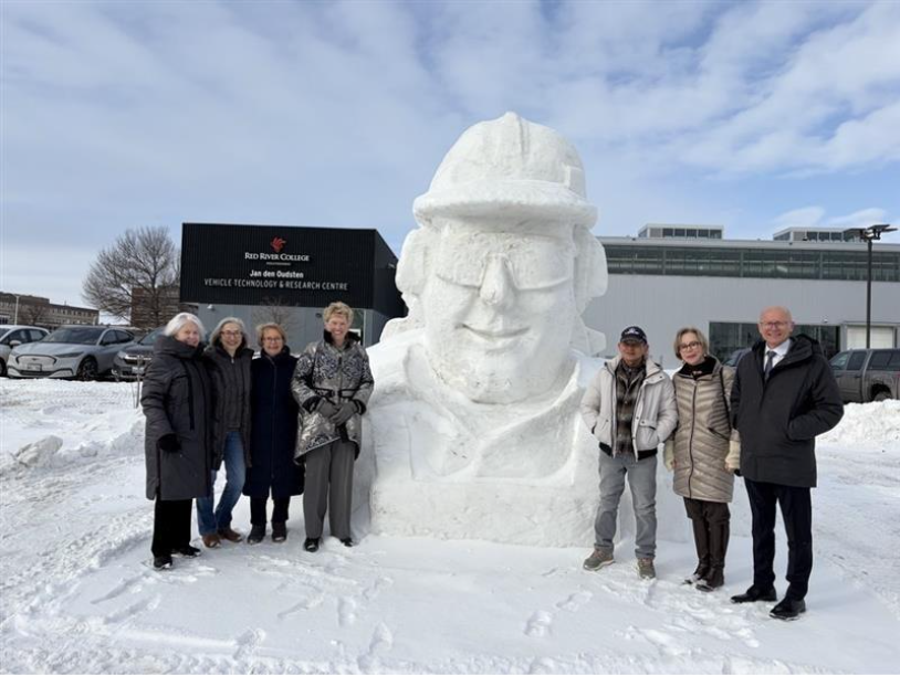 Seven people stand next to the snow sculpture and smile at the camera.