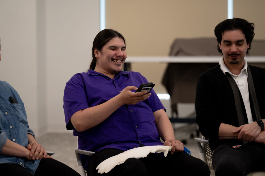 A person in a purple shirt smiles while holding a phone.