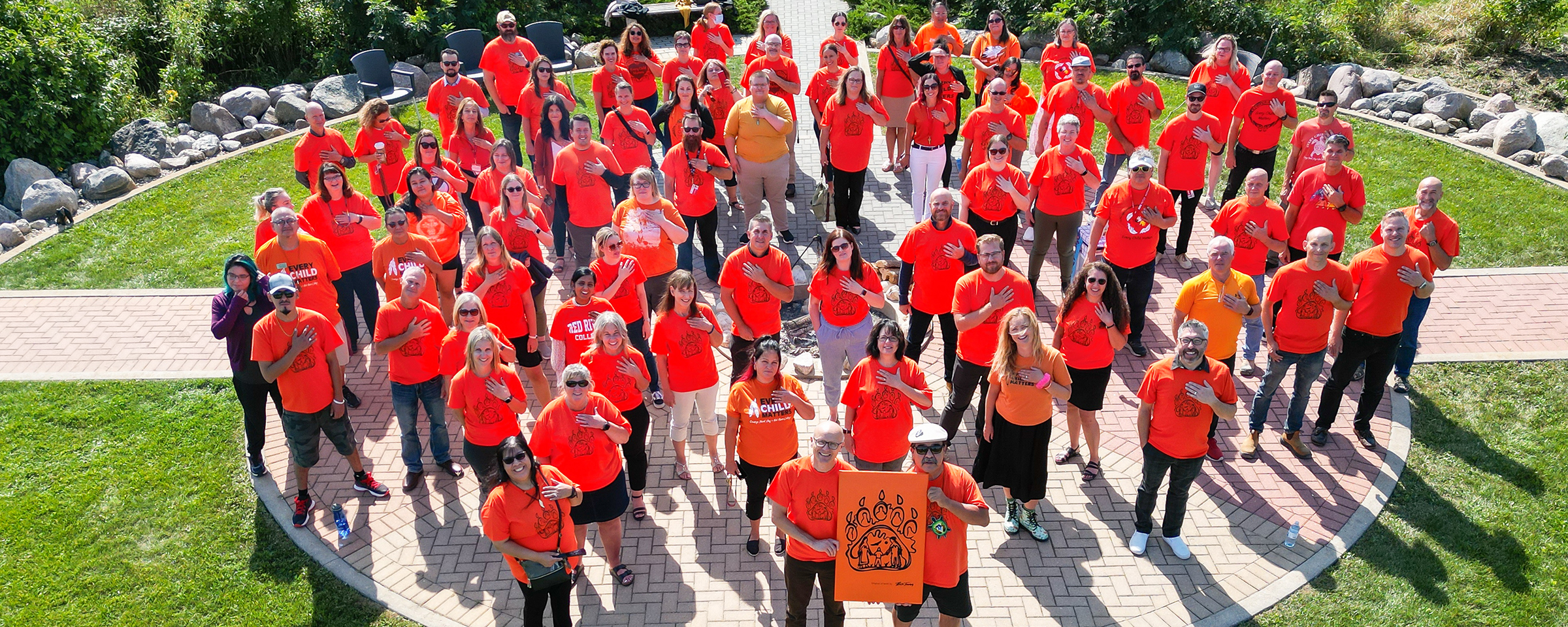 People wearing orange shirts outside, holding their hands over their hearts