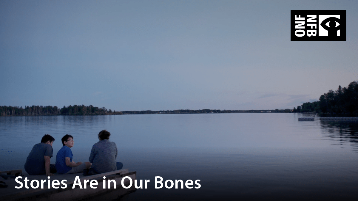 Three people sitting on the deck beside a still lake. Film title: Stories are in our bones