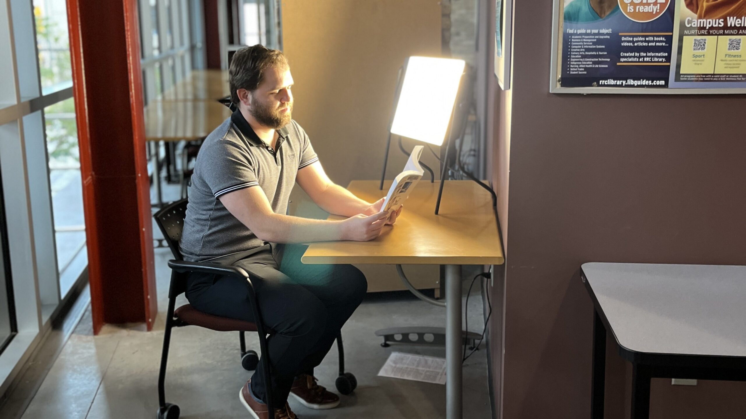 Photo of a pseron reading a book in front of a therapy light at the EDC Library