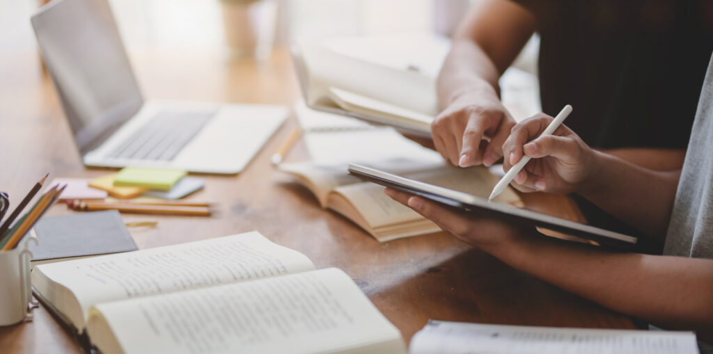 Close-up view of two people discussing their research while using tablet and books open on the table.