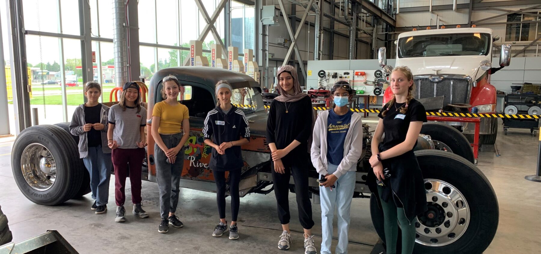 Group of girls stands in a garage in front of a car.