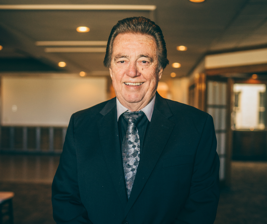 Man stands in black suit and tie.