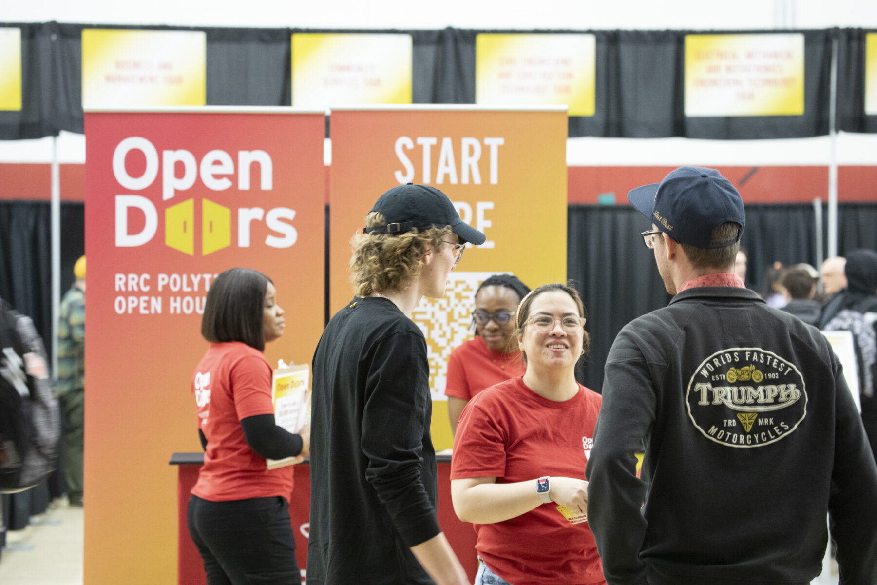 Two men talking to a volunteer wearing a red shirt at RRC Polytech's Open Doors event.