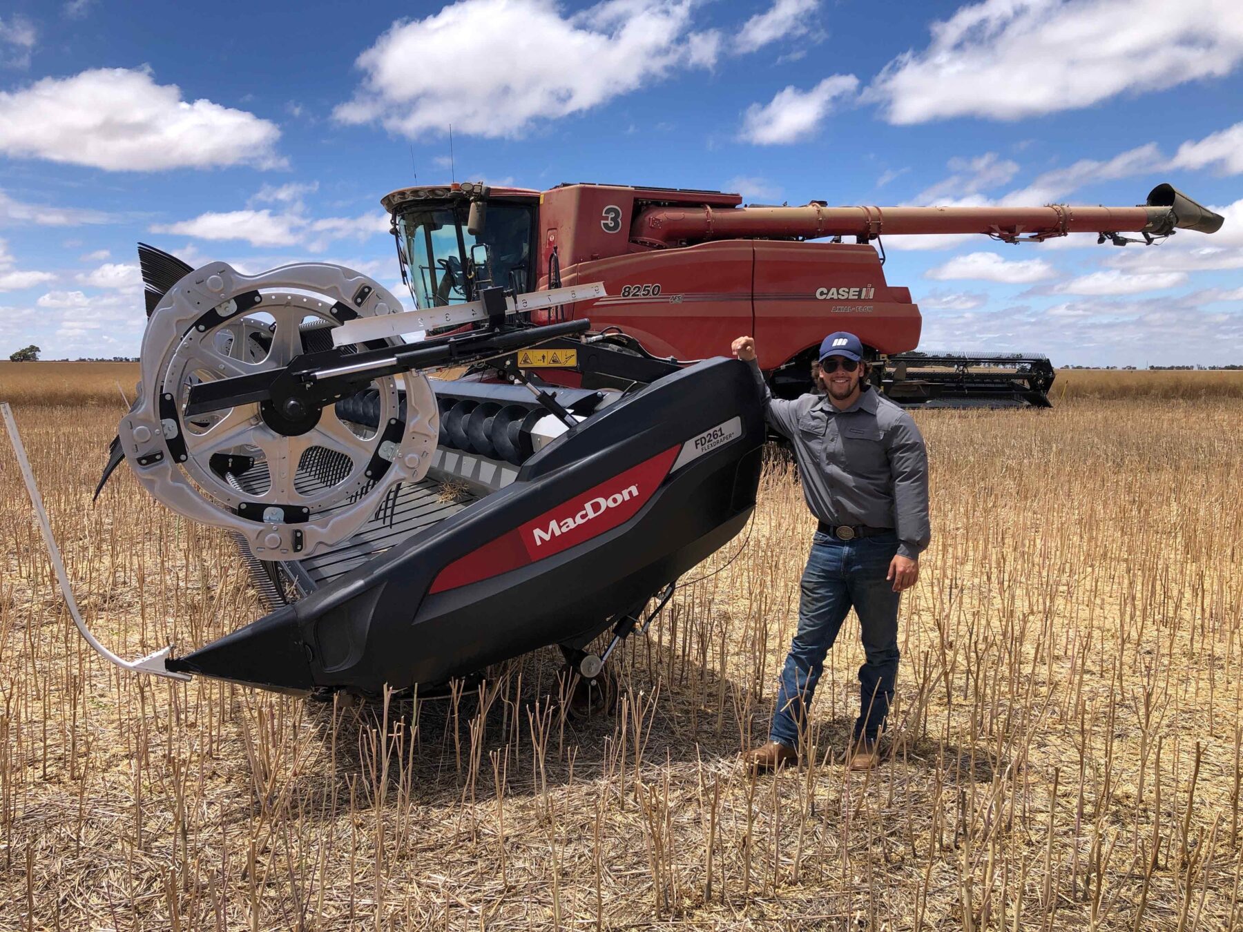 A man stands in an agriculture field with a combine.