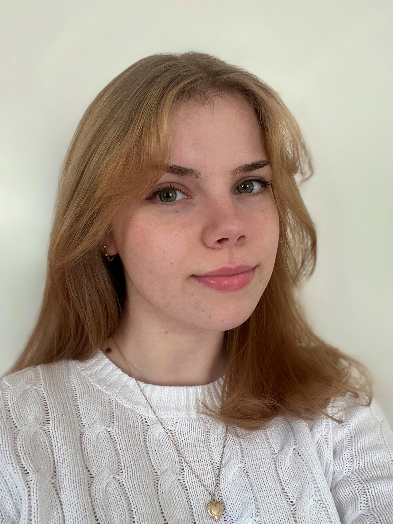 A person with long blonde hair wearing a white sweater smiles at the camera.