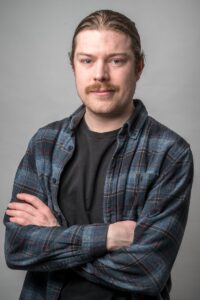 A man stands with his arms crossed, he is looking at the camera.