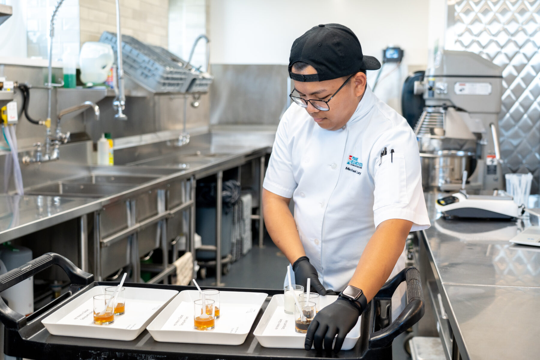 a chef-scientist in a kitchen-lab preparing trays with jars of hot honey to sample