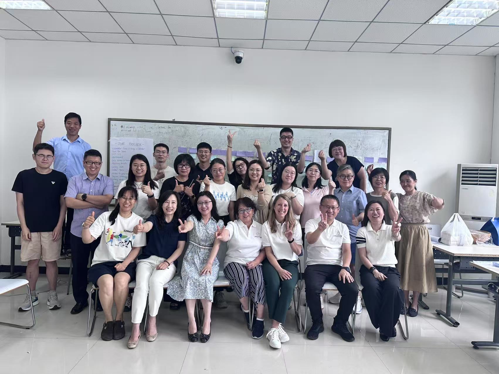 Group of people posing in a classroom, with most people making a peace sign.