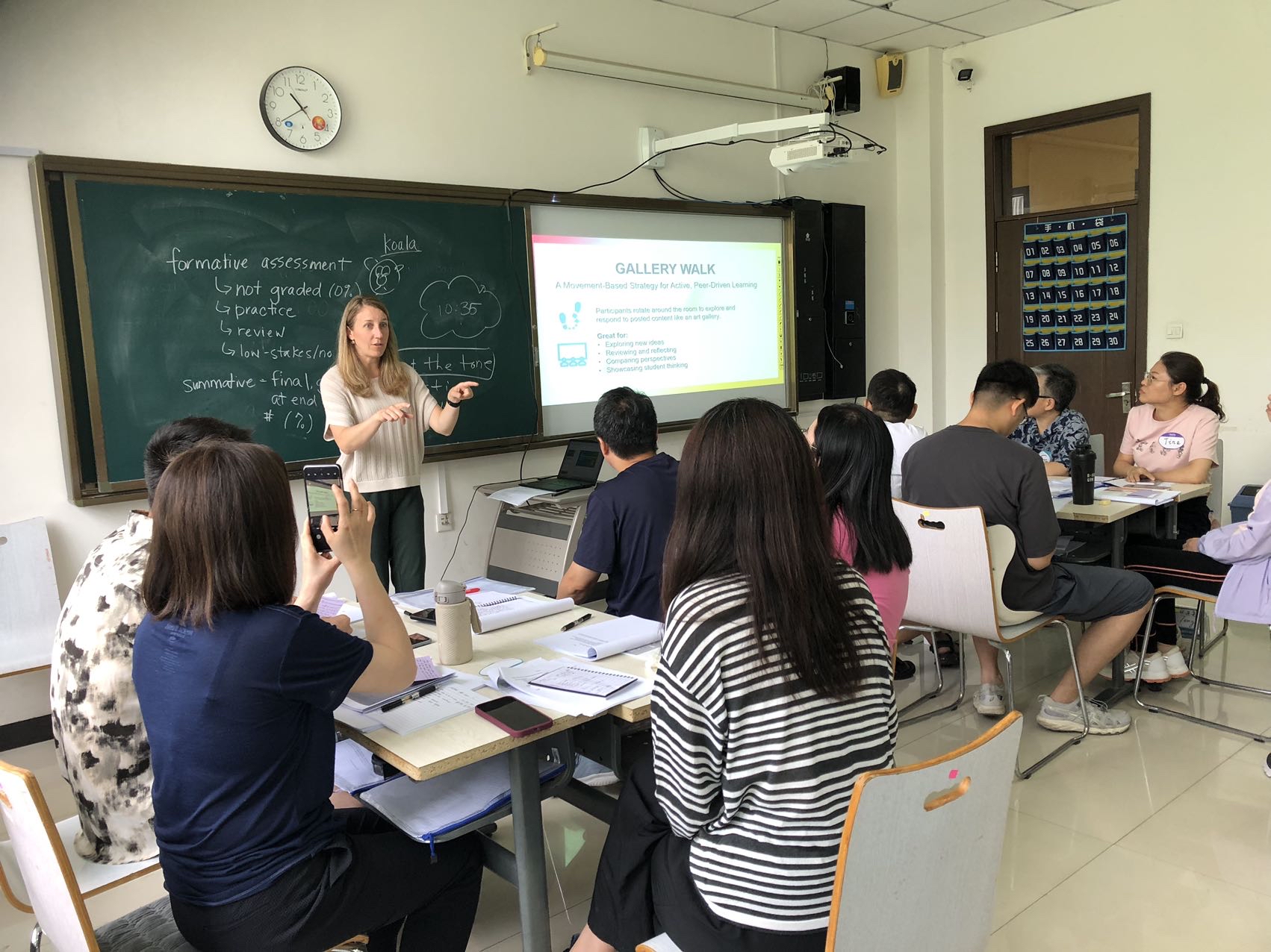 Classroom with an instructor standing in front of a chalk board and screen facilitating