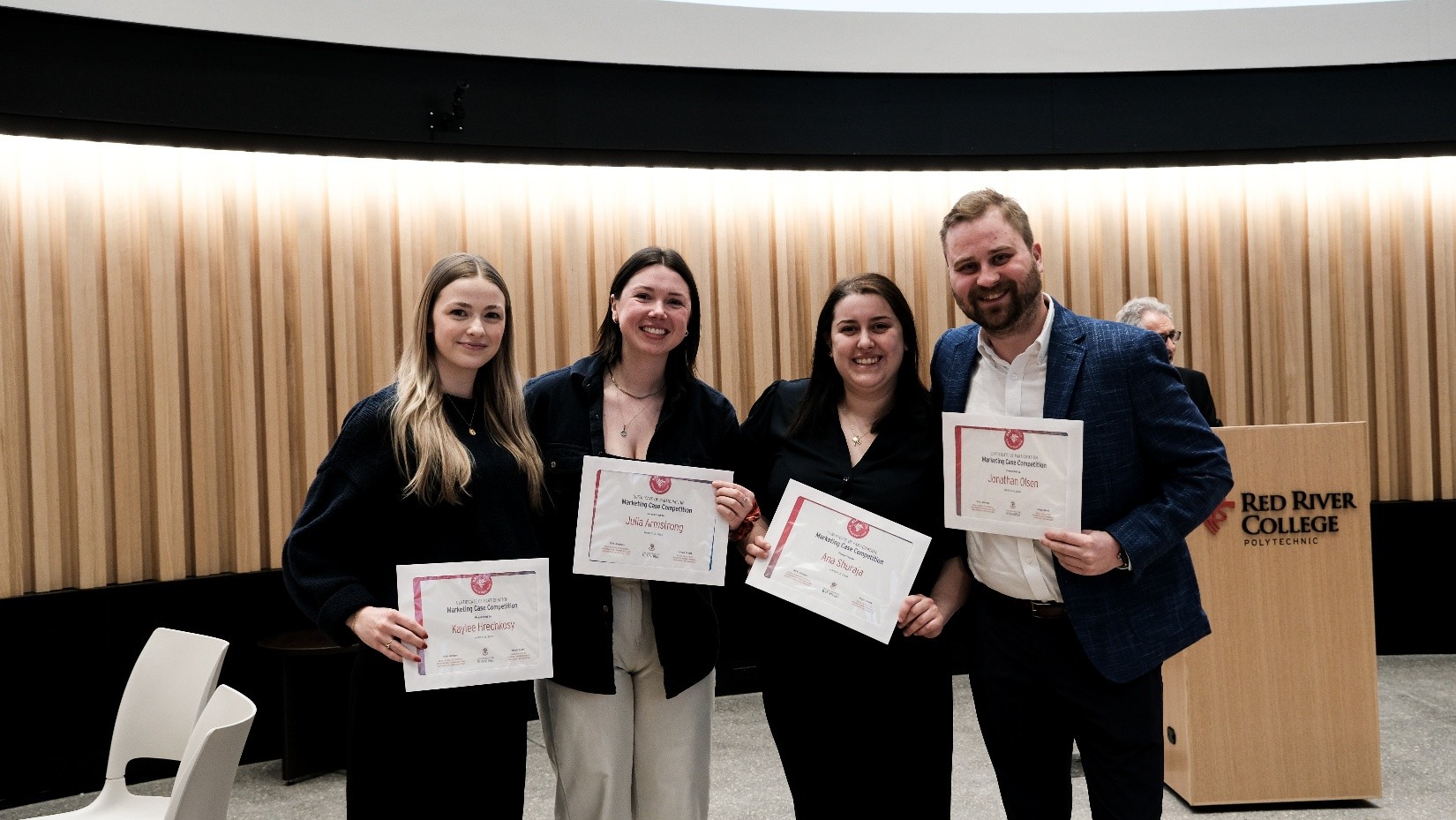 Four people hold certificates and smile at the camera.