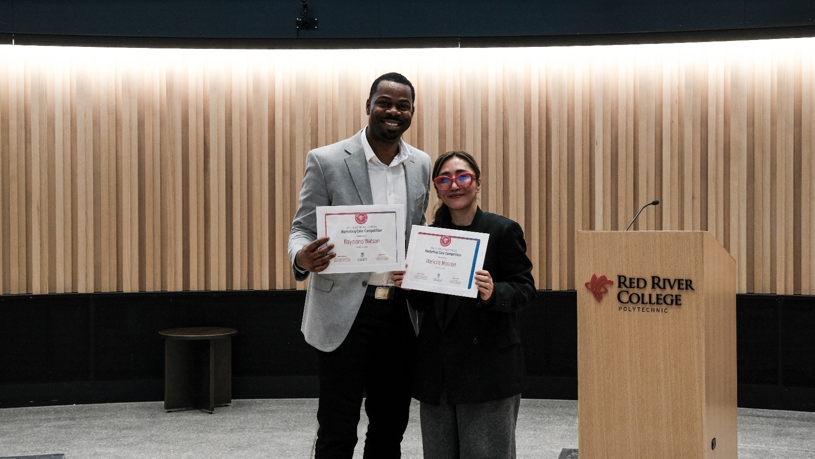 Two people hold certificates and smile at the camera.