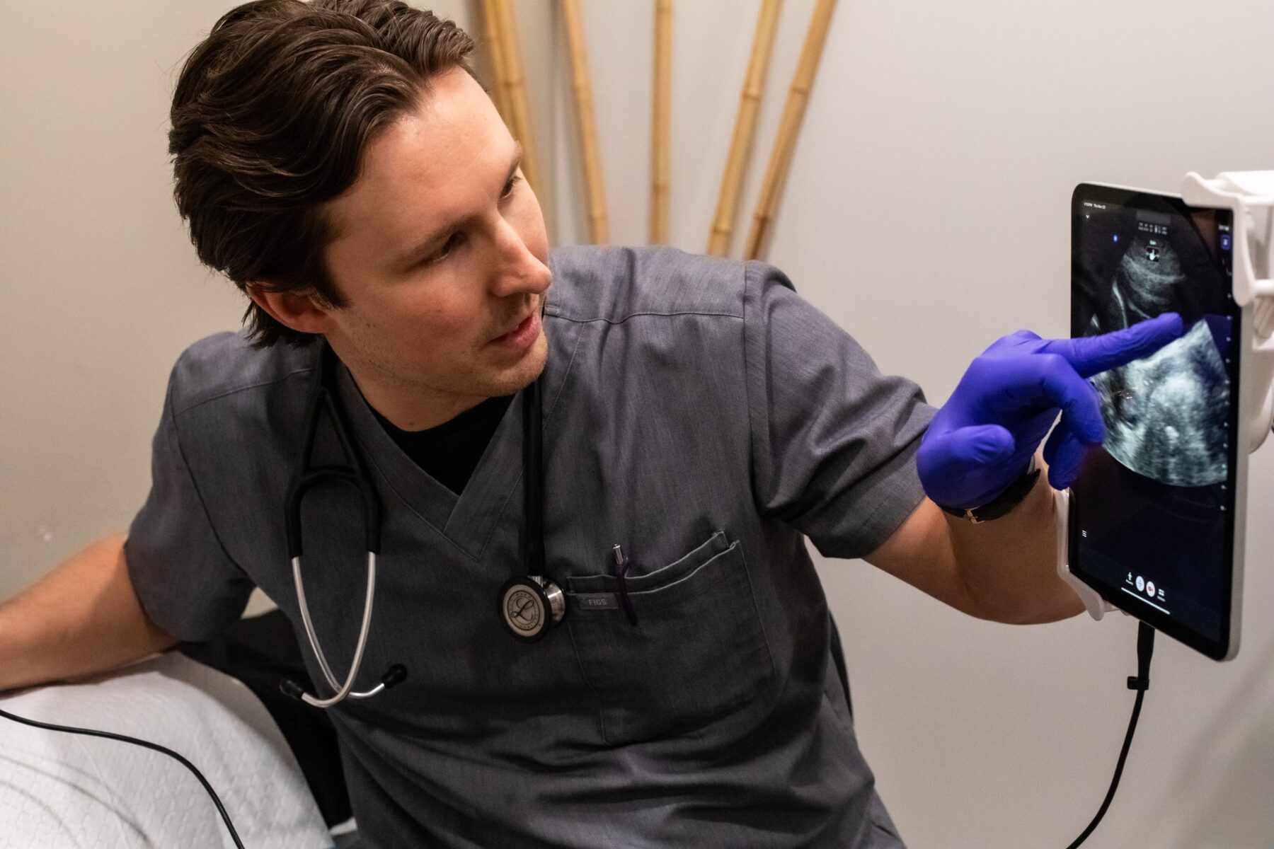 A man in scrubs is pointing at a screen, the screen shows an abdominal ultrasound