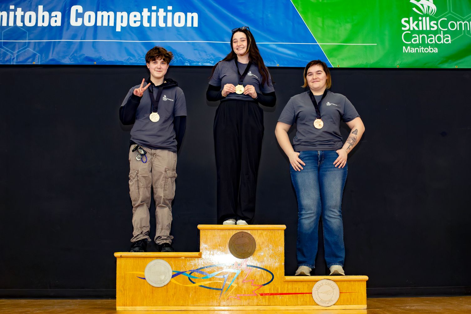 3 students posing with medals on a podium