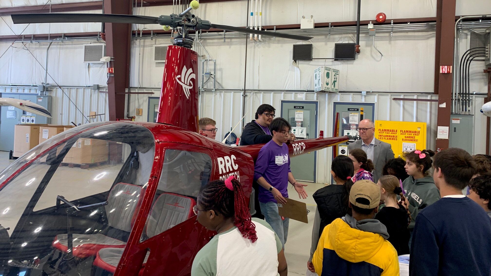 A group of students stands in front of a red helicopter.