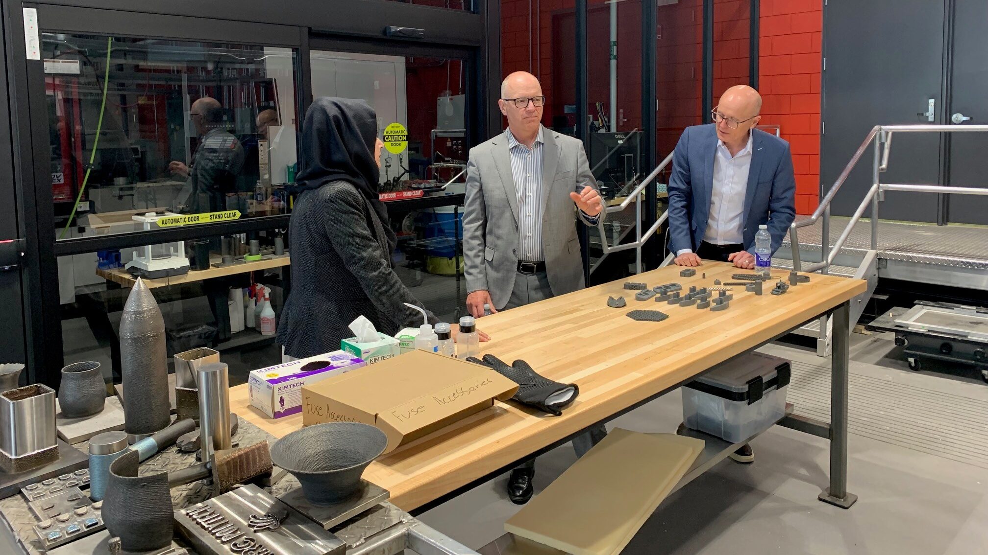 Three people stand in a lab and look at manufacturing materials.