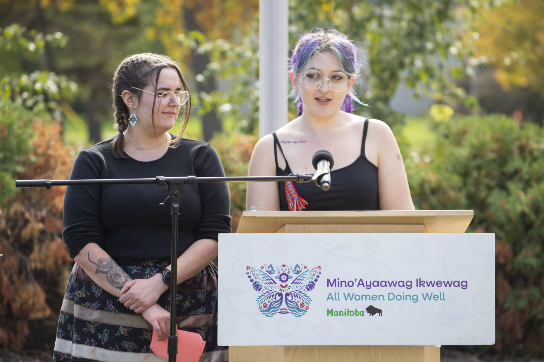 Two people stand at a podium and speak to an audience.