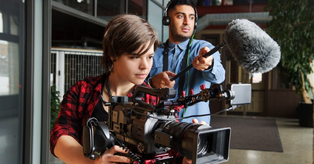 Student behind video camera, with student holding microphone