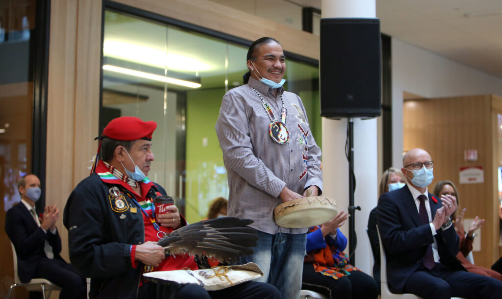 Indigenous man with drum stands for applause at opening of Manitou a bi Bii daziigae