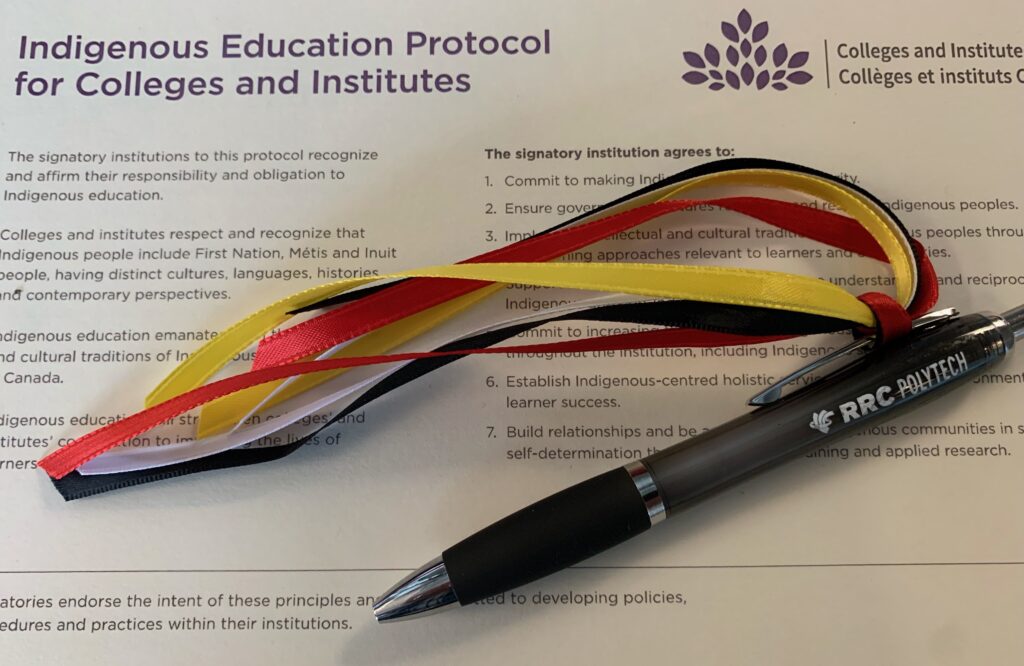 Close-up of Indigenous Education Protocol document and pen with red, black, yellow and white ribbons