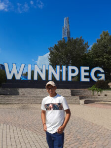 Adão Lopes da Fonseca, in front of "Winnipeg" sign at The Forks