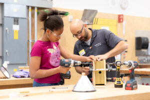 Male instructor and preteen girl using power drill in RRC Polytech's carpentry lab 