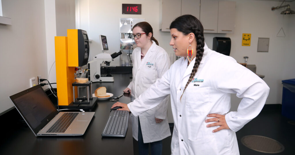 Two women in lab coats conducting lab work in RRC Polytech's Prairie Research Kitchen.