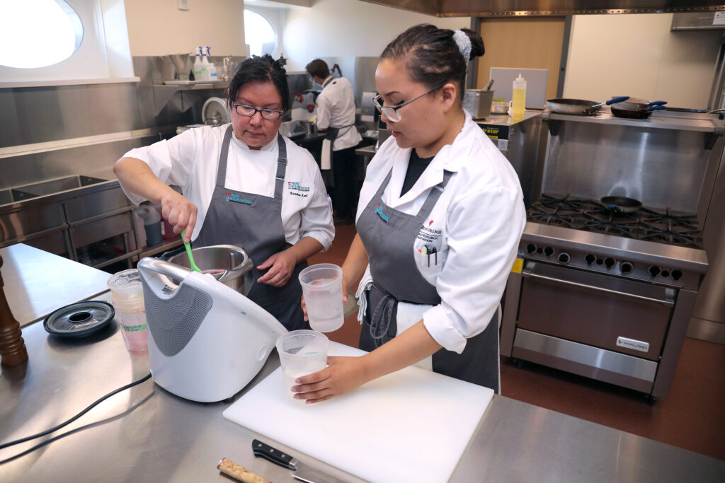 Indigenous women wearing chef's smocks and aprons, stirring ingredients inside RRC Polytech's Prairie Research Kitchen