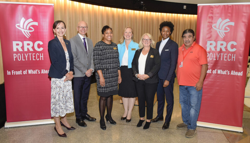 Group shot of dignitaries — including RRC President Fred Meier; Dr. Tamara Chambers-Richards, Dean, School of Health Sciences and Community Services; and Hon. Uzoma Asagwara, Minister of Health, Seniors and Long-Term Care — flanked by RRC Polytech pillars in the roundhouse auditorium.