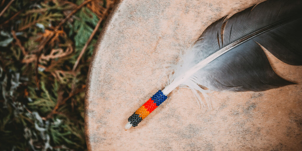 Close-up of beaded feather laid across Indigenous drum.